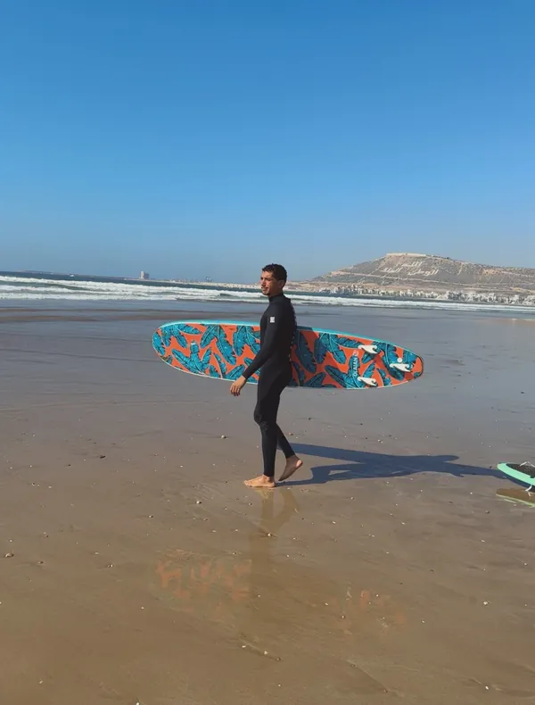 Zoubair walking on the beach with his surfboard